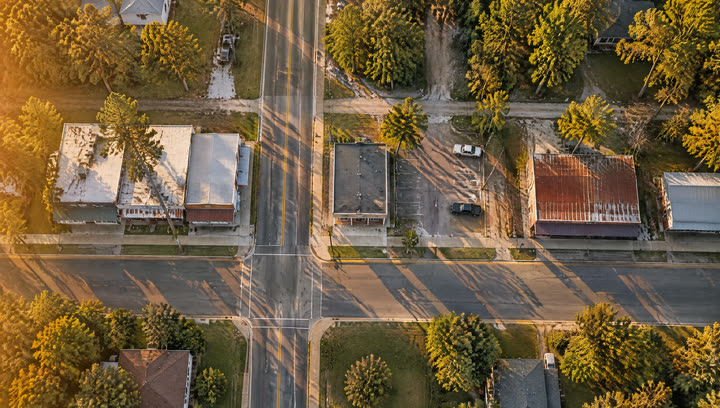 Top-down view of a crossroads lined with small single-story shops and a parking lot.