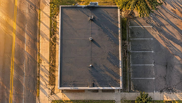 Top-down view of one small shop's flat roof beside a parking lot, marked with a map pin.